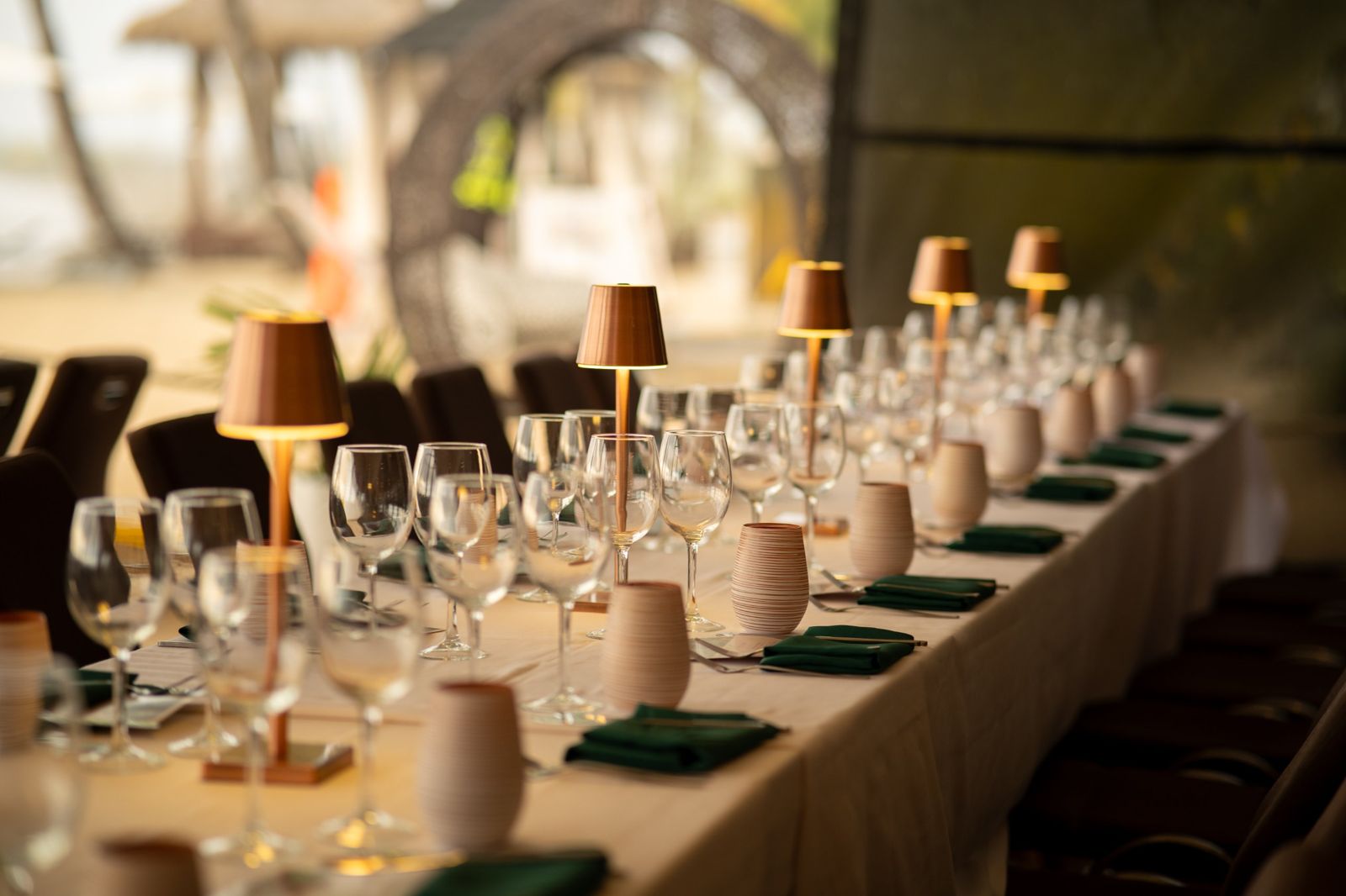 Long dinner table set with glassware and copper lamps