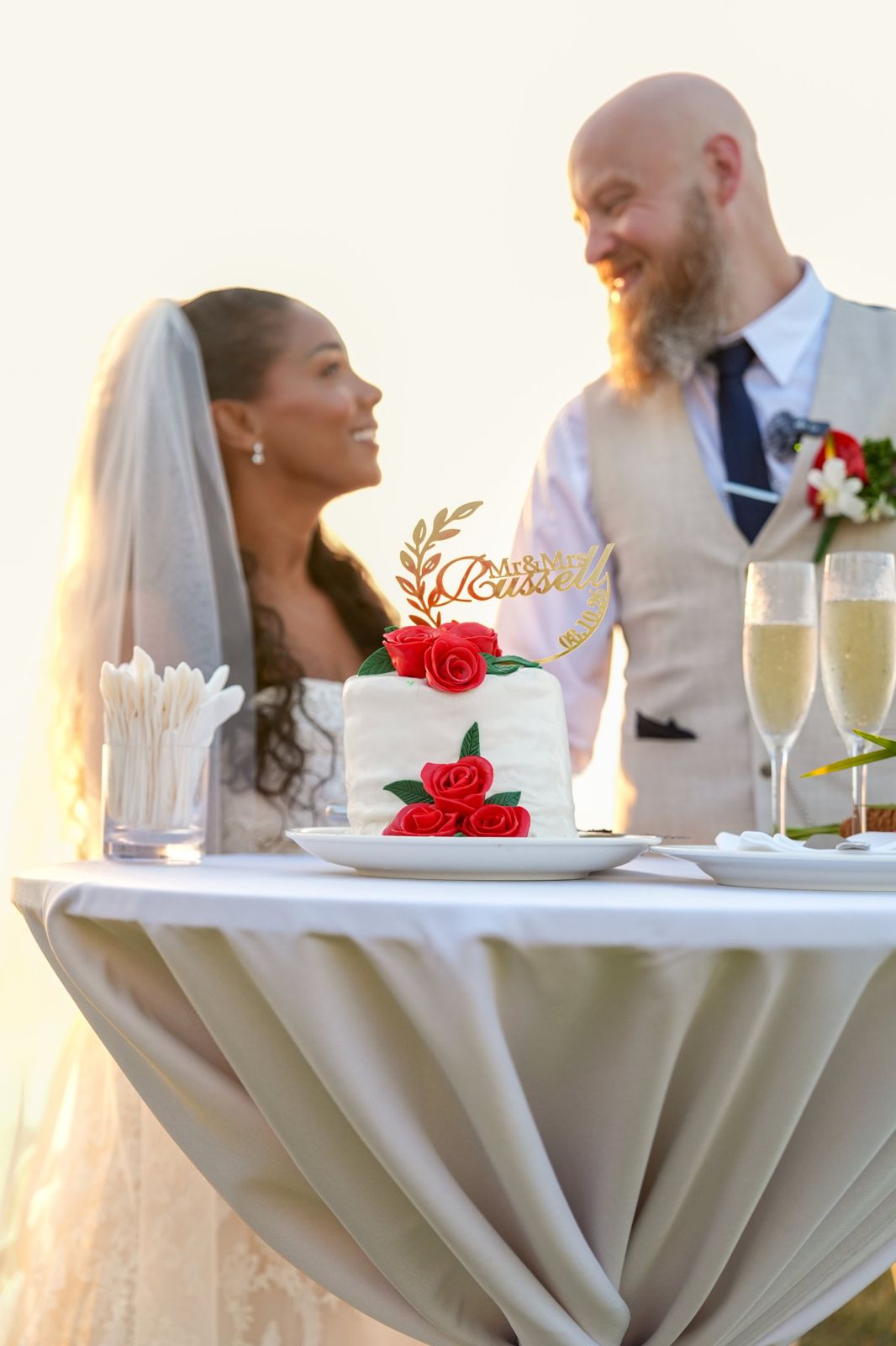 Newlyweds smiling at each other behind their wedding cake
