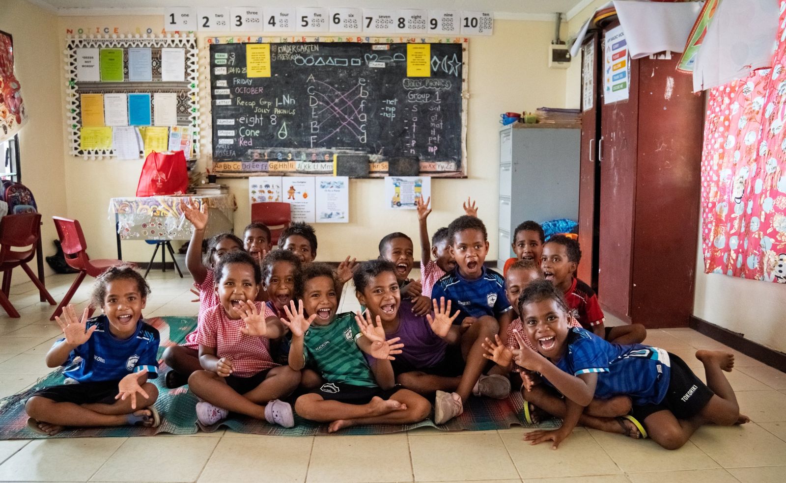 Class of young children cheering with hands raised on a classroom mat