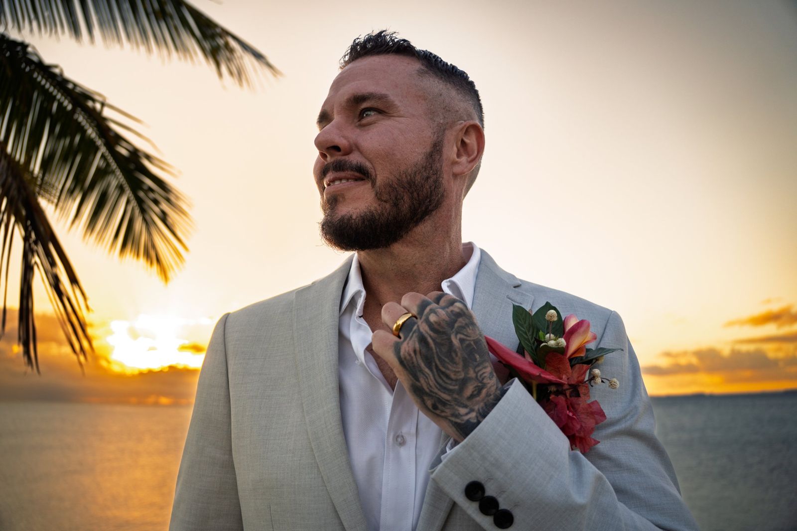 Groom in a light suit with a tropical buttonhole at sunset