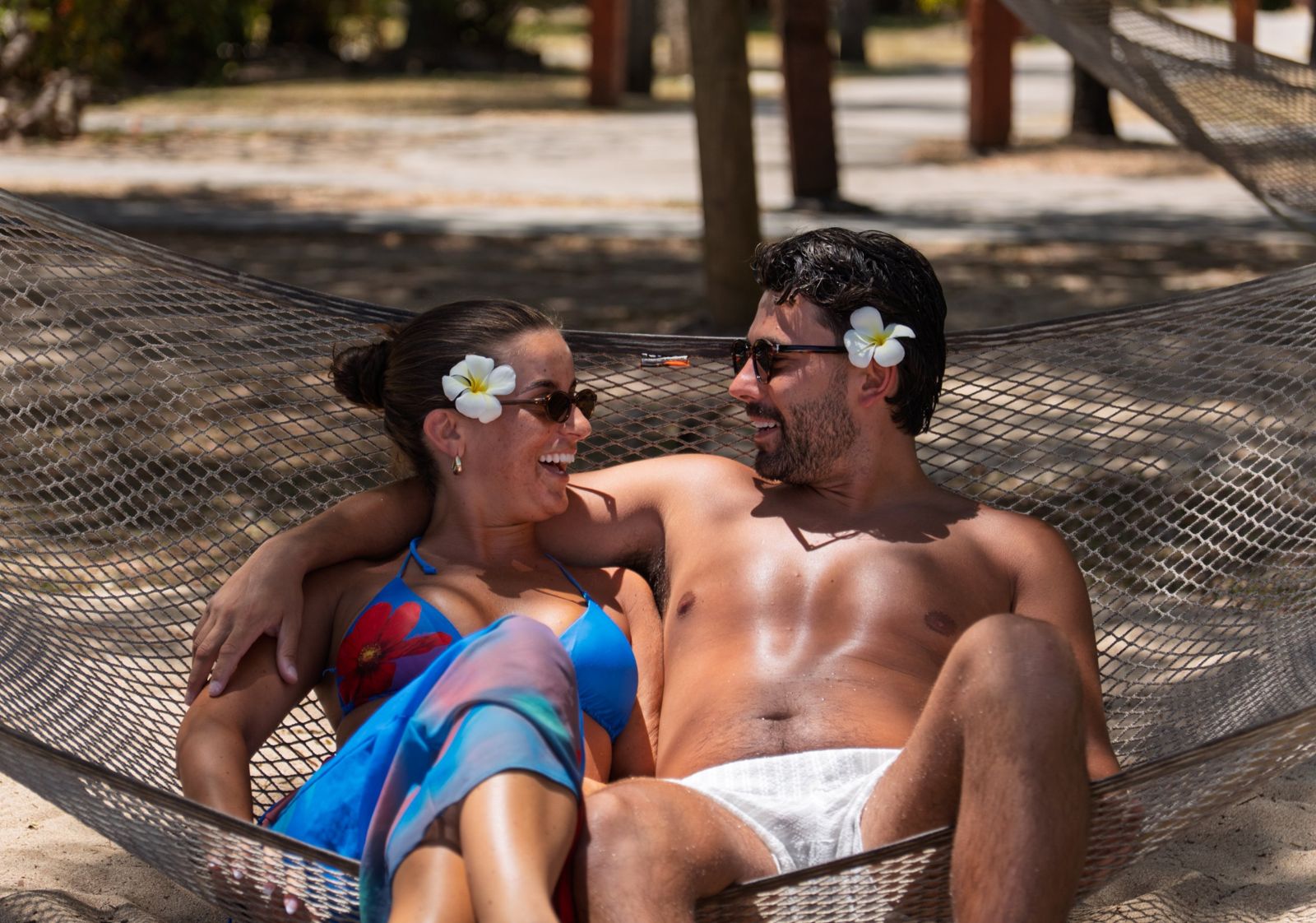 Couple laughing together in a hammock with frangipani flowers behind their ears