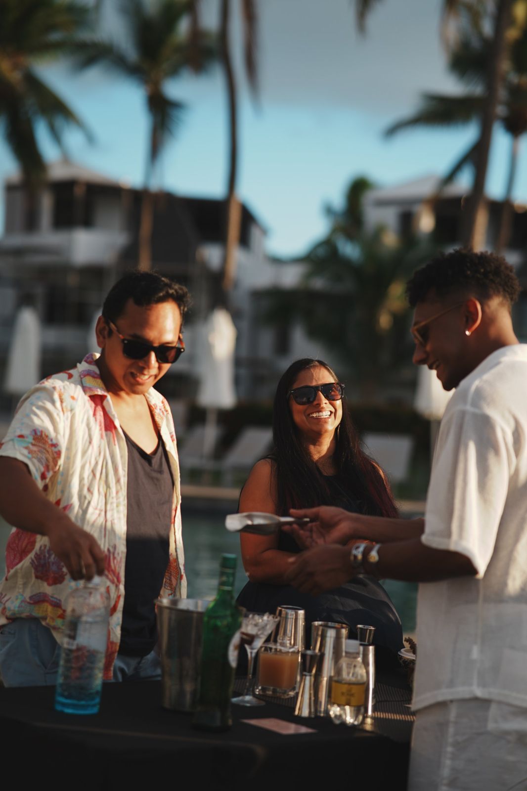 Guests laughing with a bartender at a poolside cocktail station