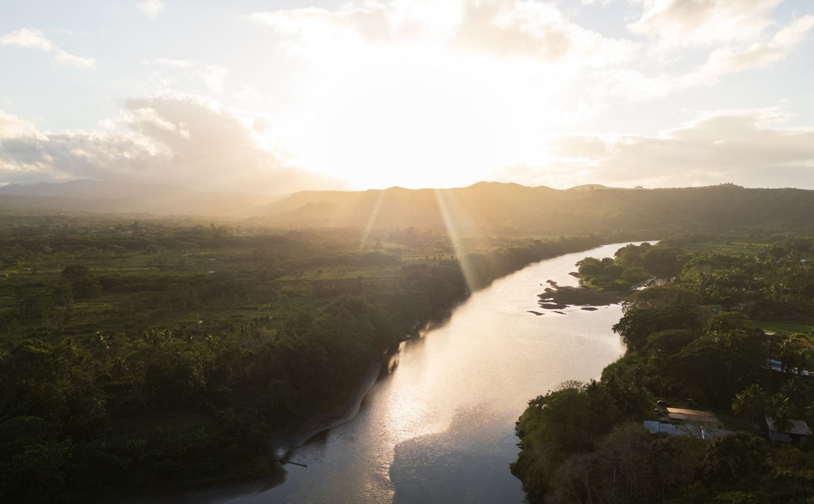 Aerial view of a river winding through green farmland at sunset